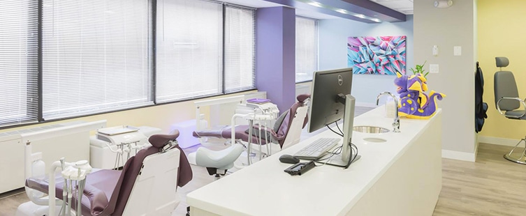 two dental examination chairs facing wall of windows covered in white horizontal blinds